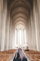 a woman standing in a large cathedral with tall arched ceiling and wooden chairs 