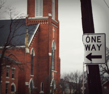 a one way sign pointing to a church 
