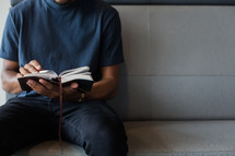 man sitting on a couch reading a Bible 