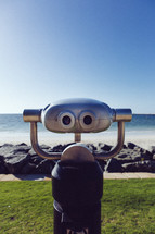 A robot stands in front of a rocky shore.