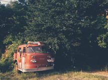 a vintage fire truck covered in an overgrown yard 