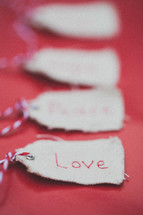Christmas gift tags lined up in a row, the first one reading "Love," on a red background.