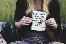 Woman's hands holding a sign which reads "Not all those who wander are lost." -- A J.R.R. Tolkien quote.