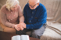 an elderly man and woman reading a Bible together 