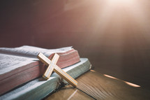 wooden cross leaning against open Bibles 