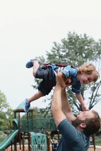 a father holding his son in the air at a playground 