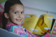 Smiling girl in pajamas reading the children's picture Bible at bedtime.