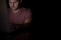A young man illuminated from the light of a computer.