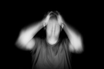 Blurred image of a man with his hands to the sides of his head.