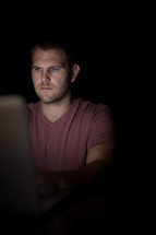 A young man illuminated by light from a computer.