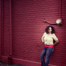 African American woman leaning against a red brick wall 