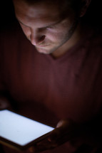 A man's face illuminated by light from an electronic tablet.