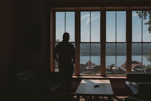 man looking out a window at a lake 
