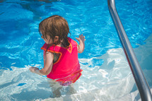 a toddler girl in a life vest in a swimming pool 
