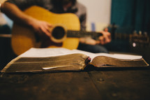 A man playing a guitar next to an open hymnal 