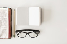 Open Bible with a pencil, journal and reading glasses for taking notes. 