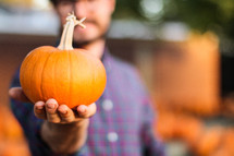 a man holding a pumpkin at a pumpkin patch 