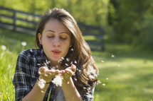 Woman sitting in a field blowing dandelion seed heads.