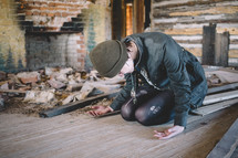 A woman kneels on the floor in prayer in an abandoned house.