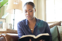 African-American woman reading a Bible on a couch