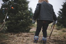 a boy child holding a saw in a Christmas tree lot 