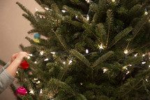 Small child's hands hanging ornaments on a Christmas tree