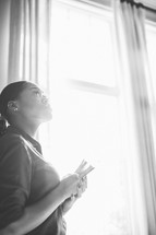 woman looking up to God near a window 