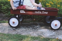 a brother and sister riding in a red wagon 