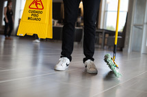 a man holding a dust mop and wet floor sign in a lobby 