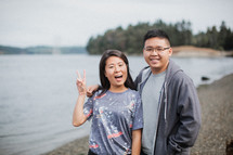 a couple standing by a river shore giving peace signs 