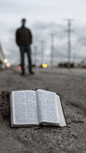a Bible on a curb and a man standing in the distance 