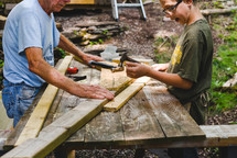 grandson helping grandfather hammer nails into wood boards 