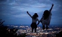 friends jumping up celebrating and view of distant suburbs at night 