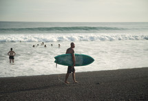 man walking down a beach carrying a surfboard 