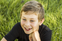a smiling boy child sitting in tall grass 