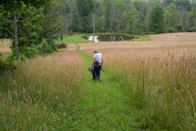 grandfather and granddaughter walking to a pond carrying fishing poles 