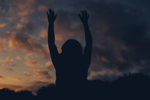 silhouette of a woman with raised hands at sunset 