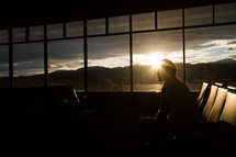 Silhouette of a man sitting by an airport window at sunrise.