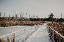 snow on a boardwalk over a pond 
