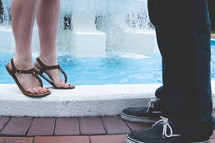 feet of a couple standing near a fountain 