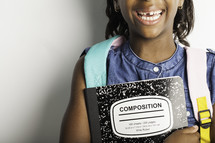 a smiling girl with missing teeth holding a composition notebook 