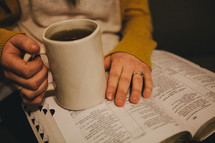 A woman holding a coffee cup and reading a Bible. 