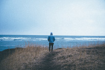 a man standing on a shore looking out at the ocean 