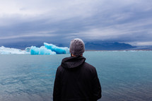 man looking out at icebergs and ice from a glacier across sea water 