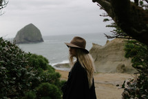 A blonde woman in a hat near the ocean.