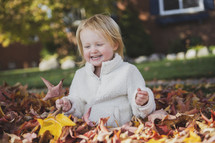a little girl playing in fall leaves 