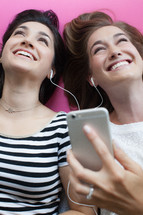 Two young women laughing and listening with ear phones.