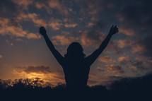 silhouette of a woman with raised hands at sunset 