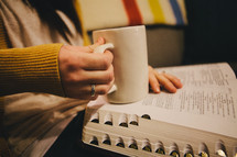 A woman holding a coffee mug and reading a Bible. 