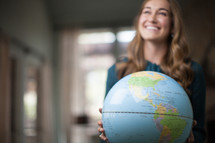 A smiling young woman holding a globe.